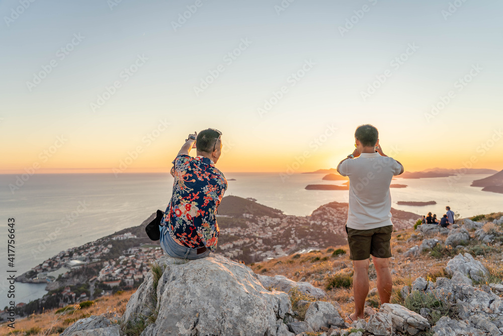 Fototapeta premium Tourists take photo of sunset over Dubrovnik old town Adriatic Islands coastline in summer from Mountain Srd