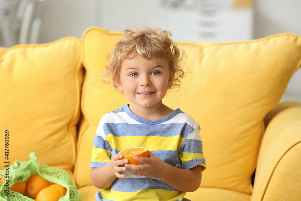 Cute little boy with orange on sofa in room Cute little boy with orange on sofa in room