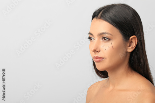 Young woman with eyelash loss problem on light background