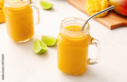 Mason jars of tasty mango smoothie on light background