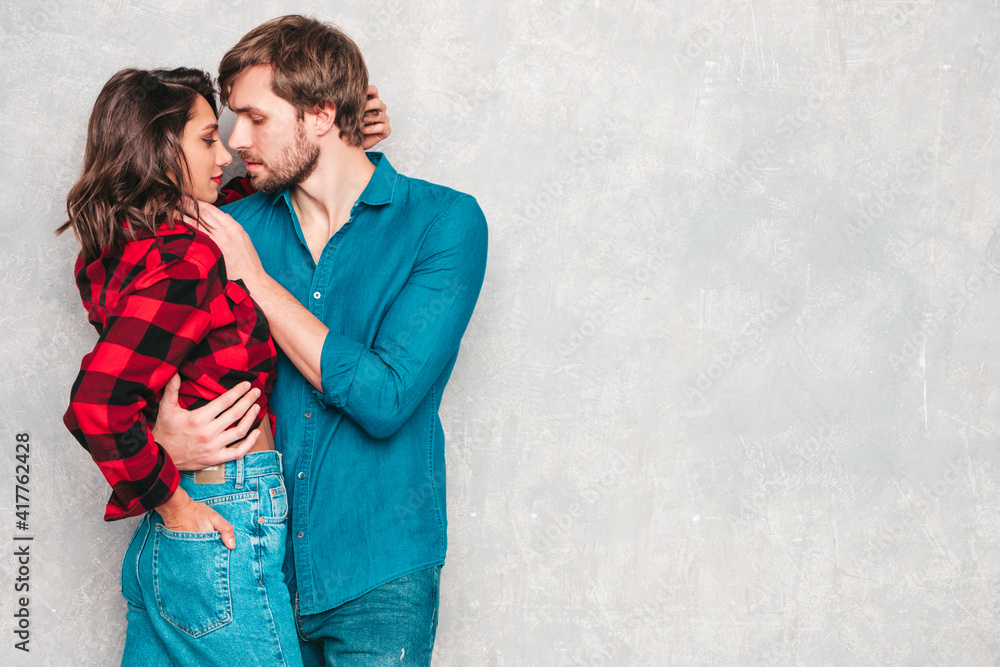 Hot beautiful woman and her handsome boyfriend. Models posing near gray wall in jeans clothes. Young passionate couple hugging before having sex. Sensual pair getting closer for kiss. Lover couple