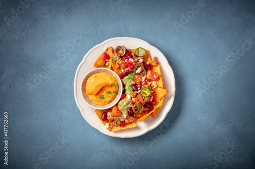Mexican nachos with chili con carne, guacamole and cheese sauce, top shot on a blue background