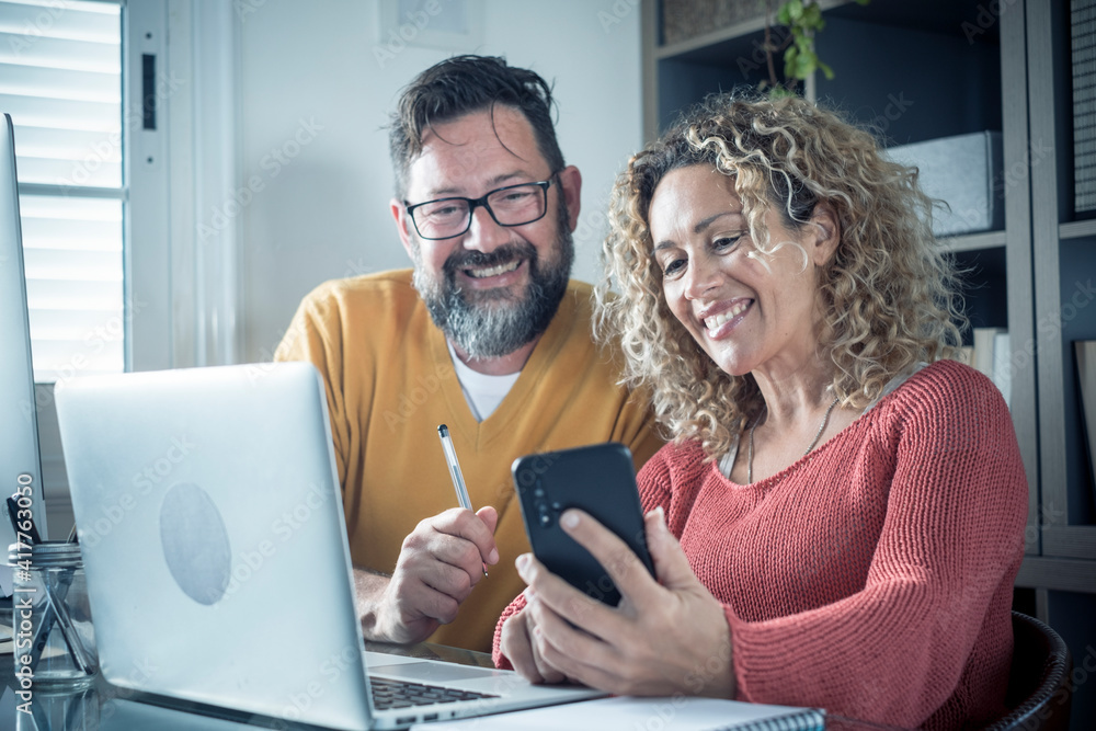 Happy man and woman couple work at home in smart working office activity together with joy - digital modern adult people in online internet job activity - cheerful female and male using computer Happy man and woman couple work at home in smart working office activity together with joy - digital modern adult people in online internet job activity - cheerful female and male using computer