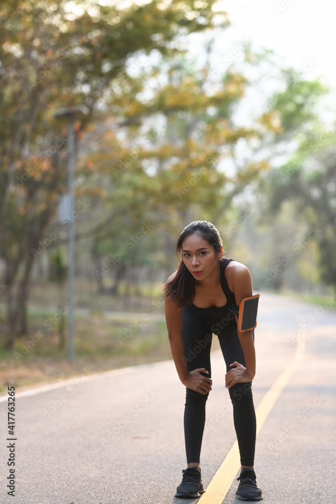 Portrait of young woman in sportswear taking a break during  jogging at park.