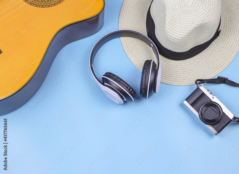 flat lay of camera, hat, headphones and acoustic guitar on blue background. - obrazy, fototapety, plakaty 