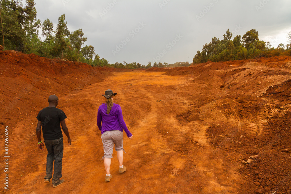 Two people walk through red dirt road