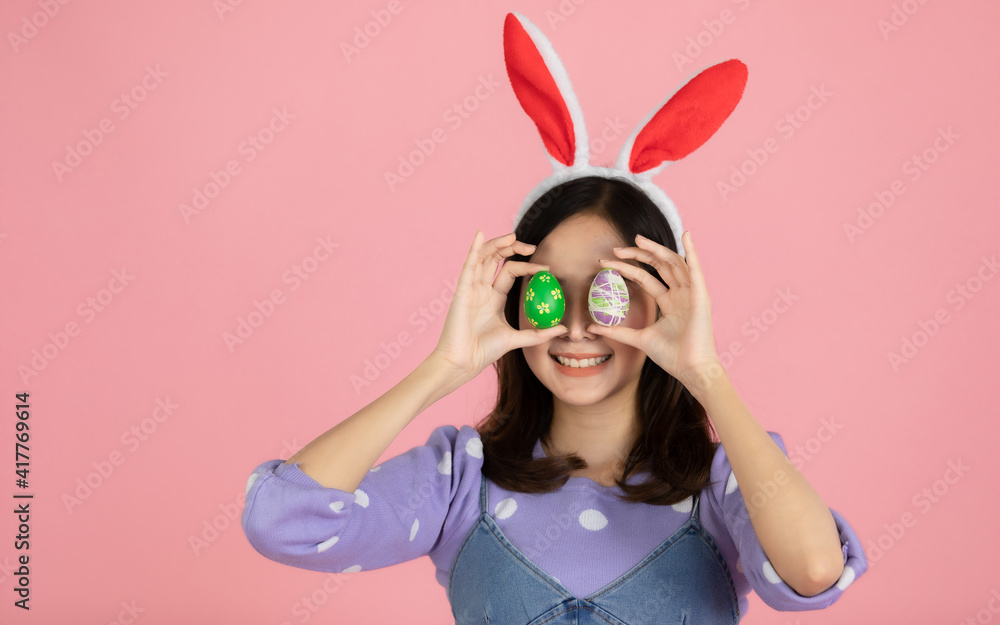 Asian woman wearing a bunny headband. Hand holding Easter eggs and covering two eyes with a smiling face. Asian woman wearing a bunny headband. Hand holding Easter eggs and covering two eyes with a smiling face.