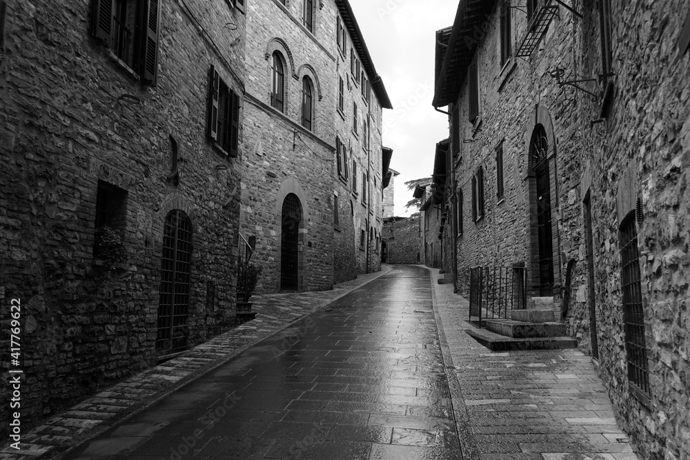 Assisi historic street with buildings built from stone after rain, black and white photo, Italy