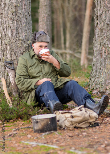 a forester in the forest drinks tea at rest, blurred forest background, bonfire with a pot over it, in the autumn