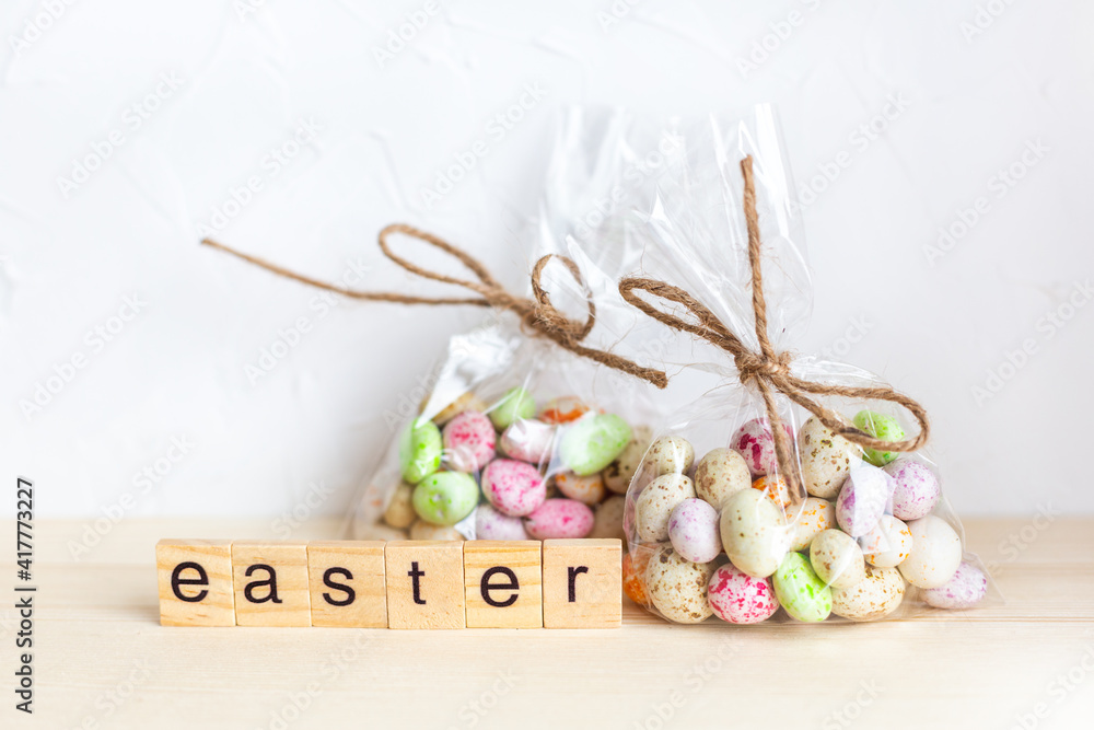 Chocolate Easter eggs in colorful glaze in a transparent bag and wooden letters on a light background. Spring holiday. Happy easter. Preparation for the holiday, gift wrapping. Sweet shop. Chocolate Easter eggs in colorful glaze in a transparent bag and wooden letters on a light background. Spring holiday. Happy easter. Preparation for the holiday, gift wrapping. Sweet shop.