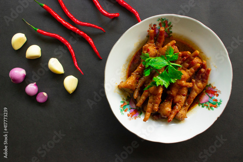 Spicy chicken feet with celery, chili, onion, garlic or ceker ayam pedas served with a white plate isolated from a black background photo