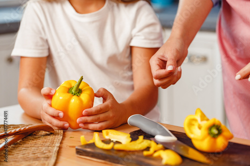 Hands of a woman and her kid cutting pepper on kitchen table
