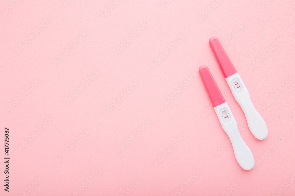 Pregnancy tests with one stripe and two stripes on light pink table background. Pastel color. Negative and positive result. Closeup. Empty place for text. Top down view.