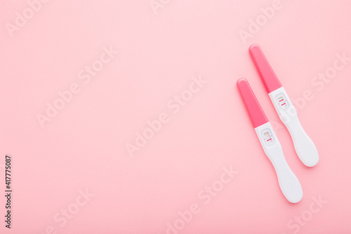 Pregnancy tests with one stripe and two stripes on light pink table background. Pastel color. Negative and positive result. Closeup. Empty place for text. Top down view.