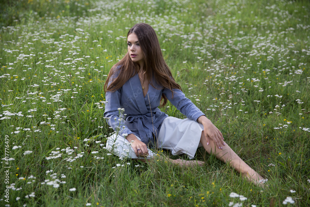 A beautiful brunette sits in a summer meadow.