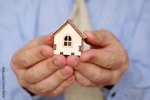 Real estate agent, wooden house in male hands. Man in office clothes with house model, purchase or rental home