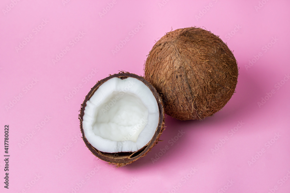Isolated coconut on a pink background. Half a coconut next to a whole coconut in the center of the image. Healthy fruit
