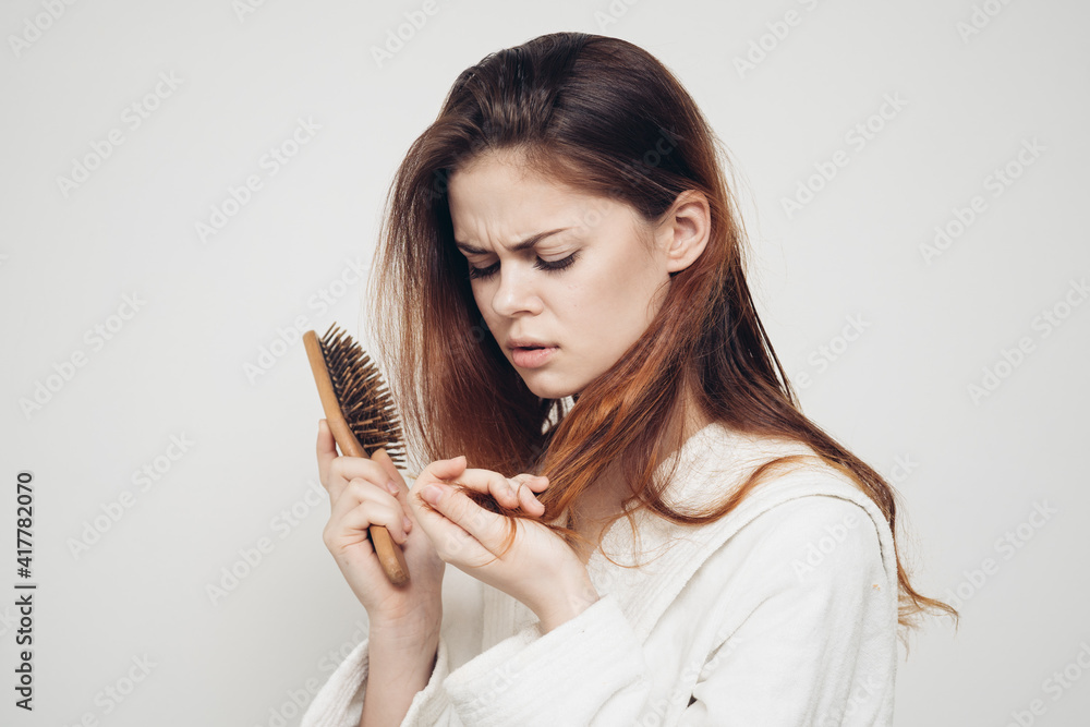 woman with a comb in her hand and in a white robe on a light background and hair loss woman with a comb in her hand and in a white robe on a light background and hair loss