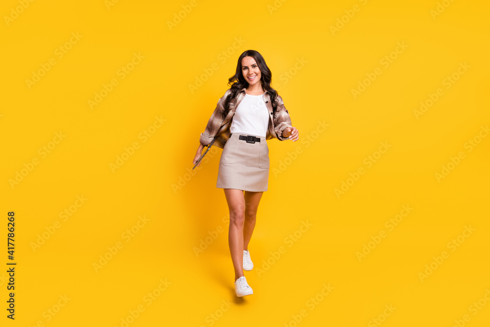 Photo of lovely cheerful lady walk look camera wear checkered coat mini skirt shoes isolated yellow color background Photo of lovely cheerful lady walk look camera wear checkered coat mini skirt shoes isolated yellow color background
