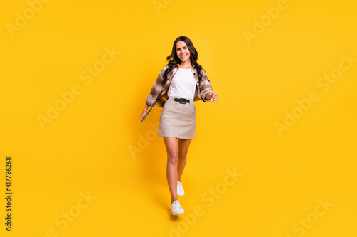 Photo of lovely cheerful lady walk look camera wear checkered coat mini skirt shoes isolated yellow color background