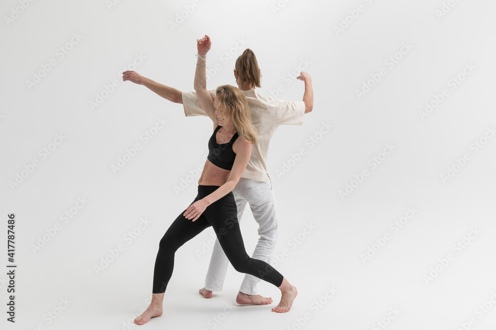 Couple of young people practicing contact yoga in studio on white background. А man and a woman lean on each other during psychological therapeutic exercise