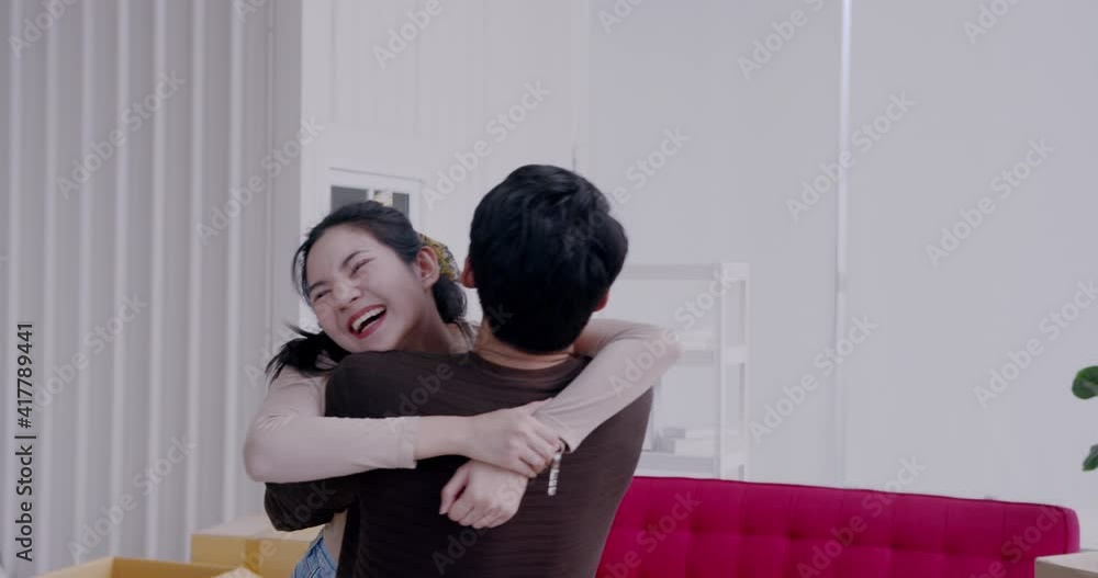 Slow motion - Happy young Asian woman tenant holds house keys in her hand and gives her boyfriend a hug with happiness on house moving day. Slow motion - Happy young Asian woman tenant holds house keys in her hand and gives her boyfriend a hug with happiness on house moving day.