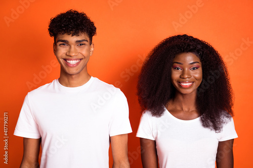 Photo of young happy cheerful positive good mood afro couple smiling wear white t-shirts isolated on orange color background