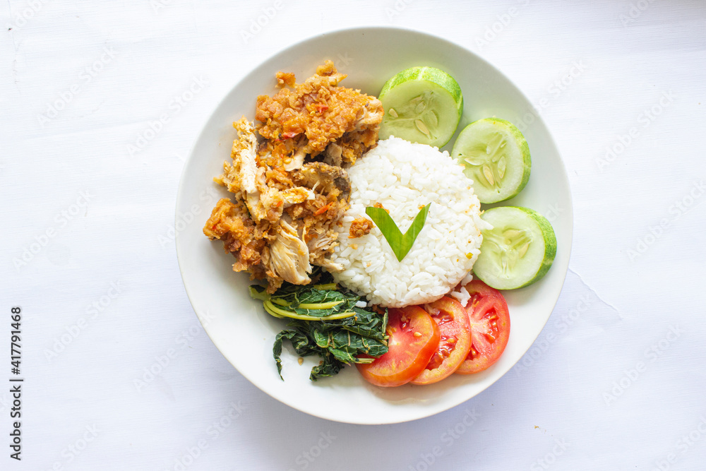 ayam geprek or chicken crush or chicken smashed is indonesian food made from made fried chicken pounded with chilli and garlic flavour and served with vegetables and rice, isolated on white background