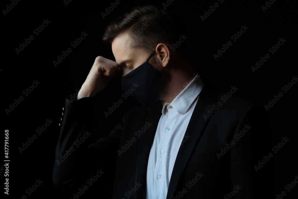 Business man with protective mask in stress grabbed the head with hand isolated on a dark background. Business man with protective mask in stress grabbed the head with hand isolated on a dark background.