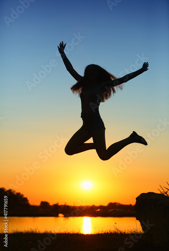 A young athletic girl jumps against the backdrop of the setting sun 