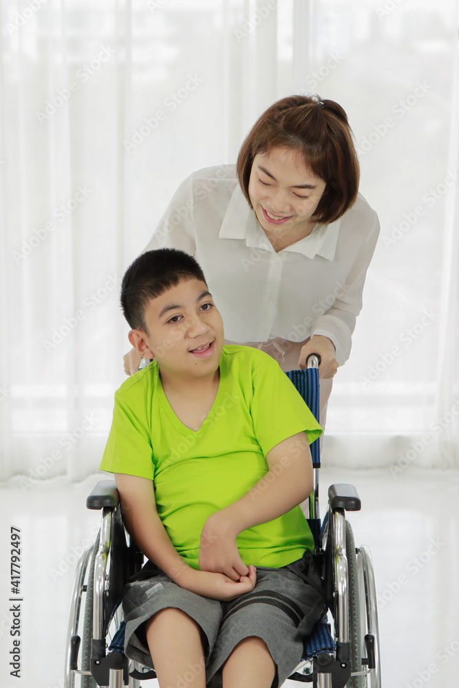 Smiling Asian nurse rolling smiling ethnic boy with disability sitting in wheelchair Smiling Asian nurse rolling smiling ethnic boy with disability sitting in wheelchair