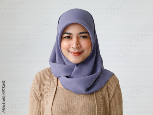 Confident young ethnic woman in Muslim headscarf smiling against white wall