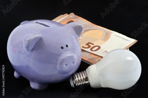 Concept de dépenses d'électricité avec une tirelire à côté d'une liasse de billets de banque sur fond noir photo