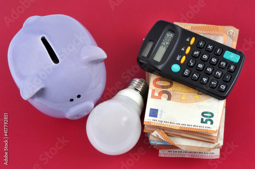 Concept de dépenses d'électricité avec une tirelire à côté d'une liasse de billets de banque et d'une calculatrice vus de dessus sur fond rouge