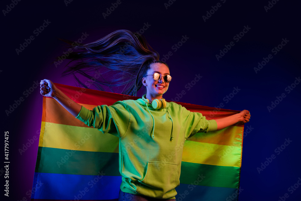 Photo of charming happy proud young woman hold rainbow flag lgbtq fly hair isolated on neon background