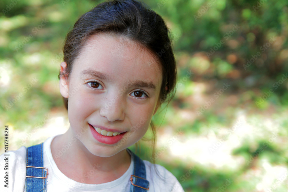 Portrait of a girl in a summer park against the background of trees. The girl rejoices in the holidays. Portrait of a girl in a summer park against the background of trees. The girl rejoices in the holidays.
