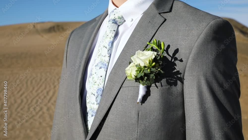 Groom Wearing Boutonniere On Grey Suit With Floral Tie. - close up