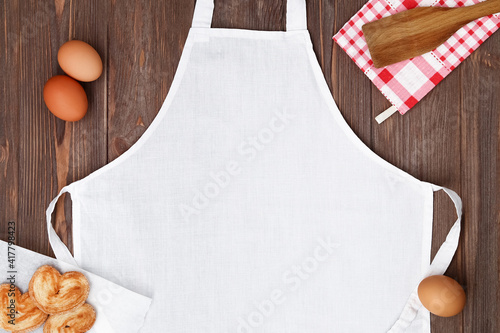 Fotografia Blank white apron template on wooden table with cookies and eggs, copy space