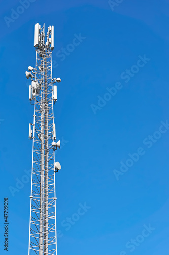 4G and 5G transmitters on a telecommunications tower. Cellular base station with white transmitting antennas on a high pole against a blue sky. Vertical image with copy space. 