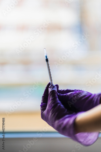 Hands with purple gloved nails hold a syringe