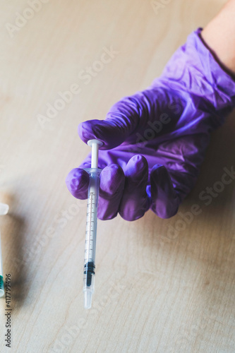 A hand of a nurse wearing purple gloves holds a syringe