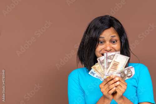 close up of a beautiful young african lady holding some money in her hand, with a look of surprise on her face