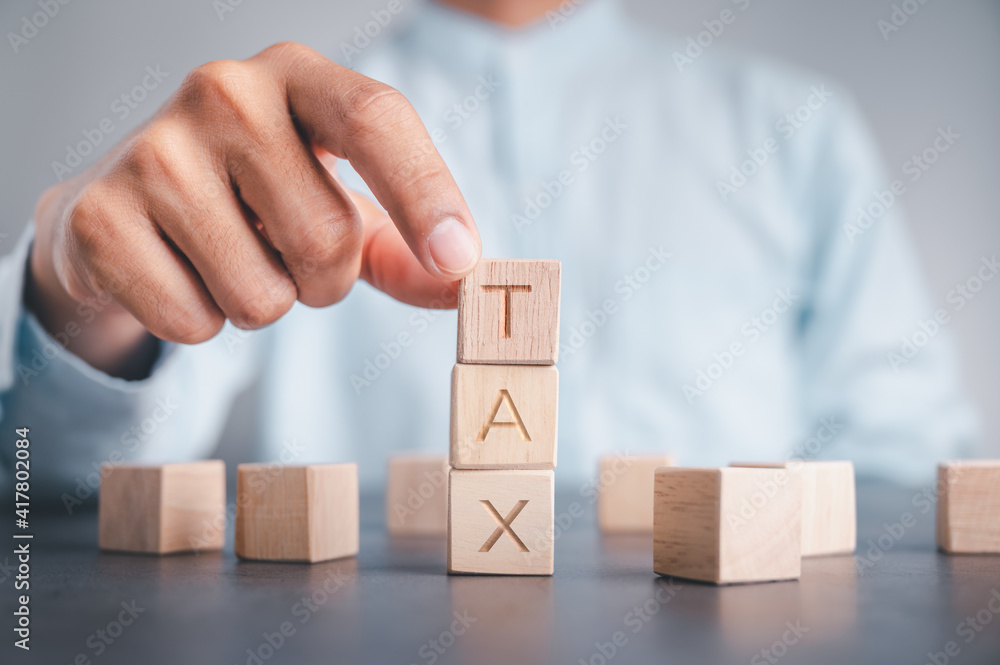Businessmen wear a white shirt at their desks in the office. Use your hand to pick up a wooden cube inscribed with the word tax. Businessmen wear a white shirt at their desks in the office. Use your hand to pick up a wooden cube inscribed with the word tax.