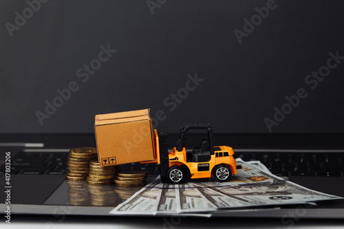 Mini model of forklift with boxes and money on keyboard. Logistics and delivery concept.