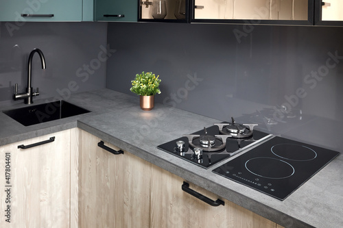 Upscale modern flat design Aqua Menthe kitchen in luxury home with induction electric hob flat oak or walnut wooden panels with flower in vase and sink with tap mixer of modern design.