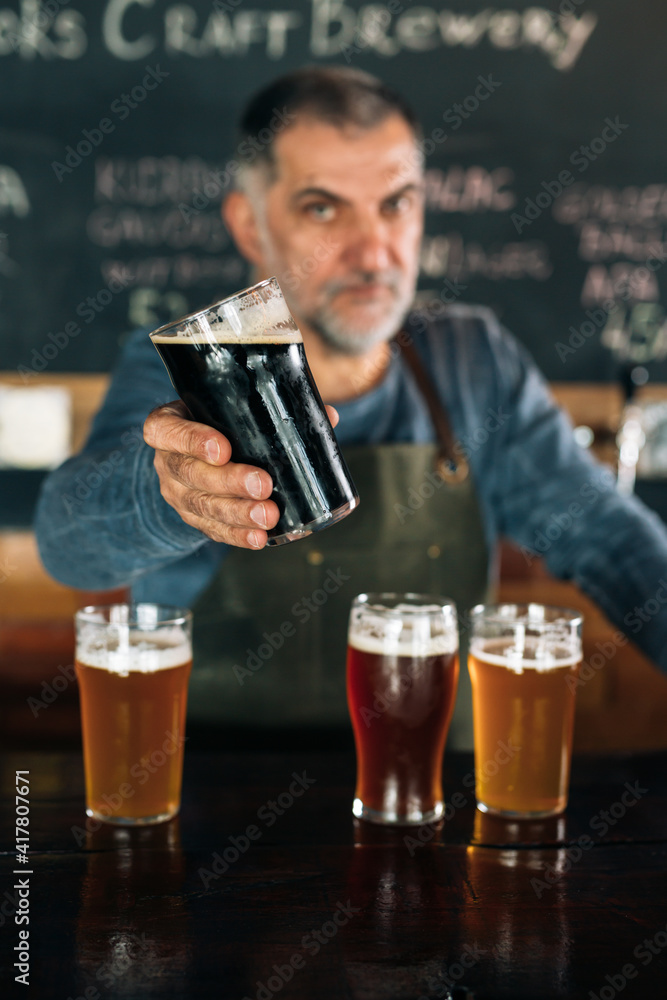 barman standing in bar. He is serving craft beer barman standing in bar. He is serving craft beer