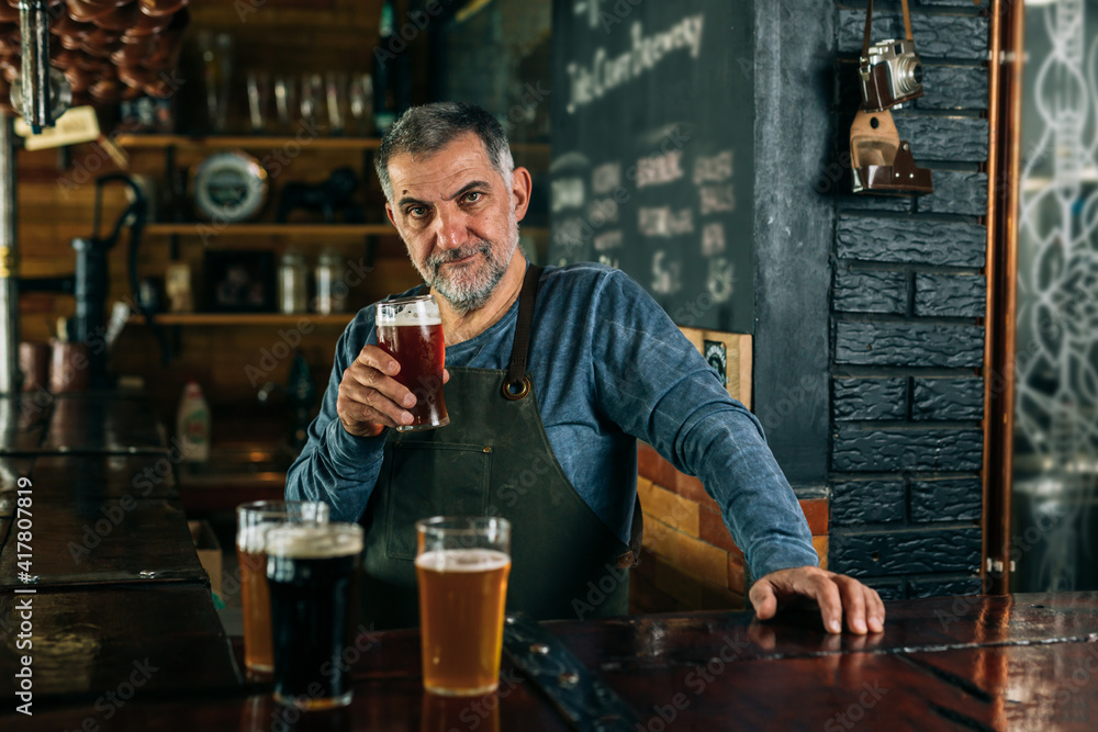 barman standing in bar. He is serving craft beer
