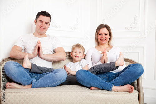 Happy family with young son in yoga pose on sofa