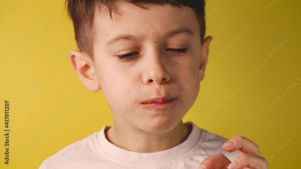 Little boy eating tortillas on yellow background. Kid eats potato chips, salty food for snack or party. Child eating junk unhealthy food. Little boy eating tortillas on yellow background. Kid eats potato chips, salty food for snack or party. Child eating junk unhealthy food.