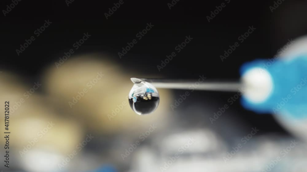 A medical syringe with a vaccine dripping from a needle. Reflection of pills drop. super macro A medical syringe with a vaccine dripping from a needle. Reflection of pills drop. super macro